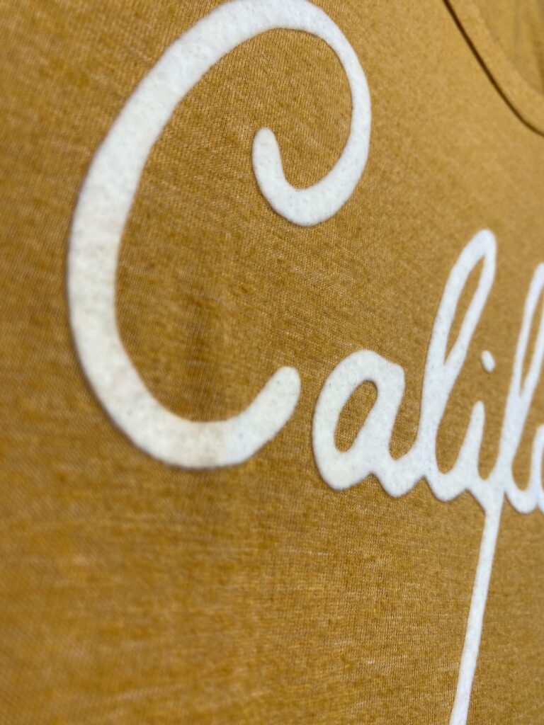 white flocked script on a mustard t-shirt