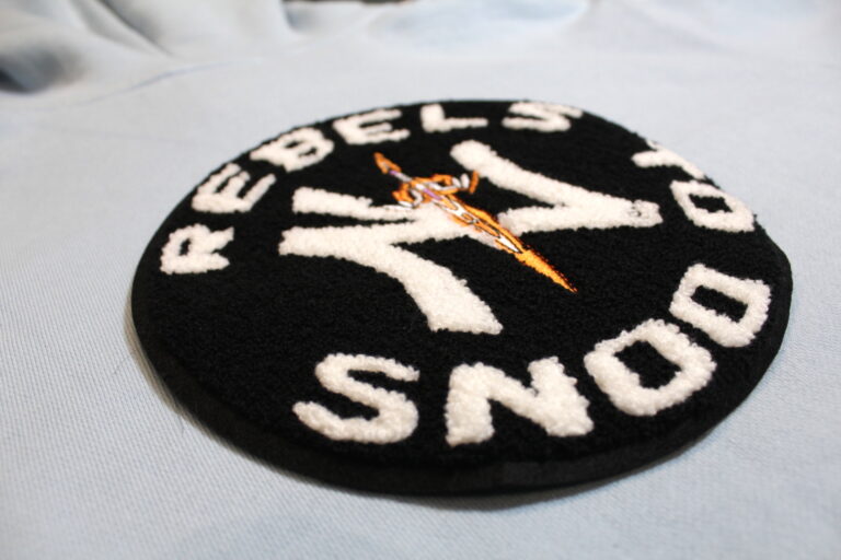 Round black chenille patch with white chenille lettering and an embroidered emblem