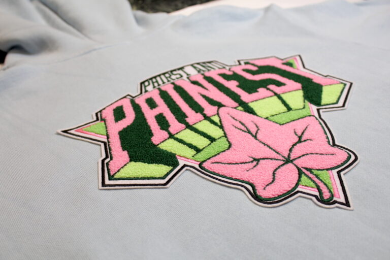 Pink and green chenille lettering patch with an ivy leaf on a light blue sweatshirt