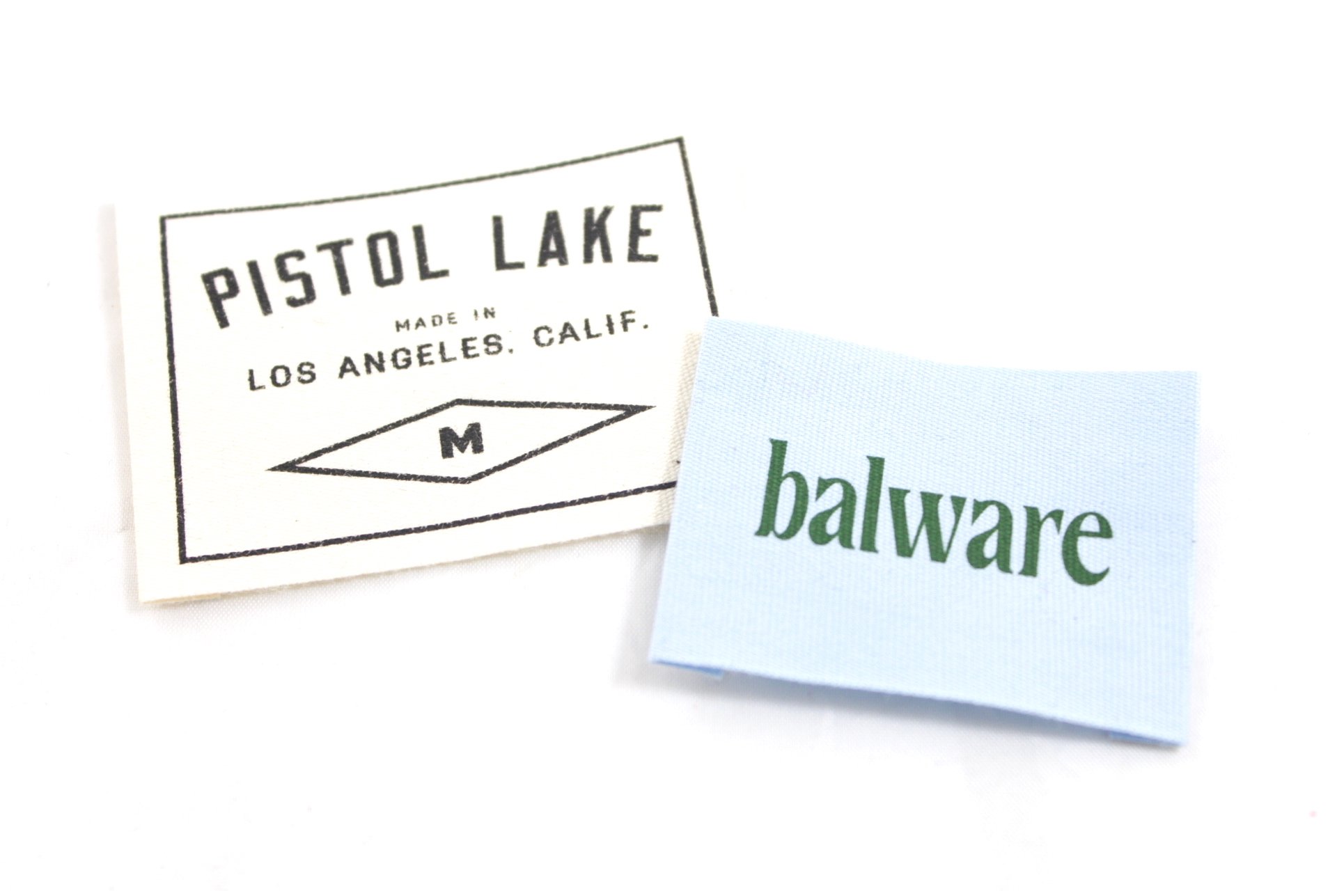 Pistol Lake white woven label next to a blue and green Balware woven label