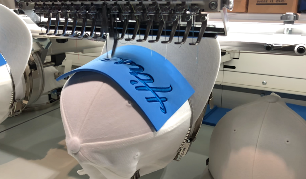 Embroidery machine stitching a puff design through foam on a white cap