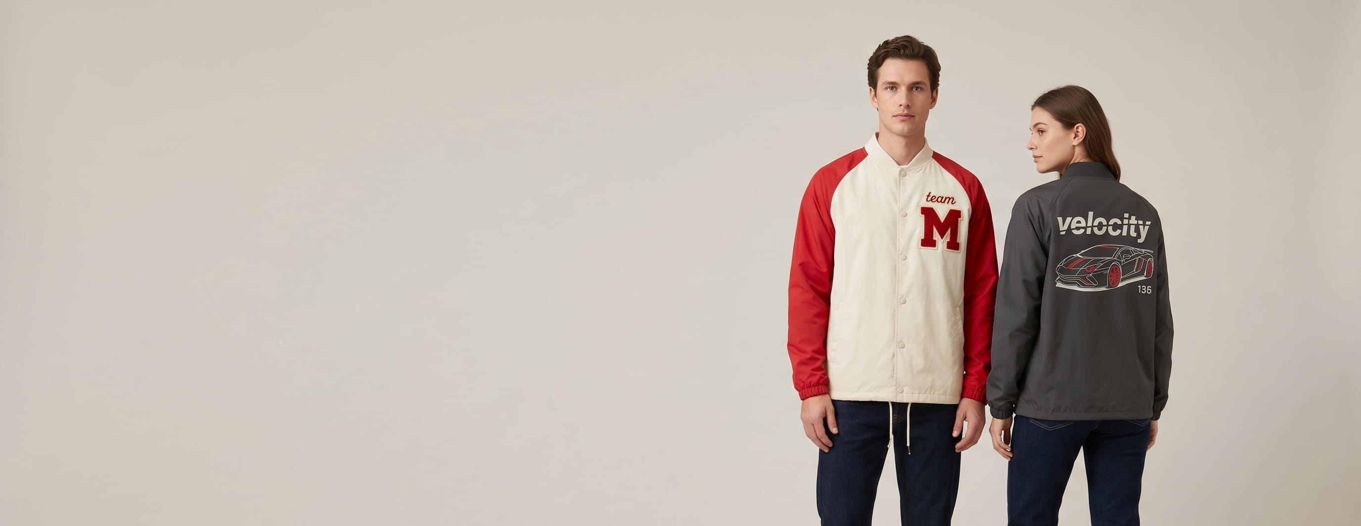 Two lifestyle models in decorated custom coach's jackets — model 1 in cream-and-scarlet color-block paneled nylon-shell coach jacket with chenille letter patch and chain-stitch embroidery + model 2 in anthracite nylon-shell coach jacket with full-back plastisol screen print
