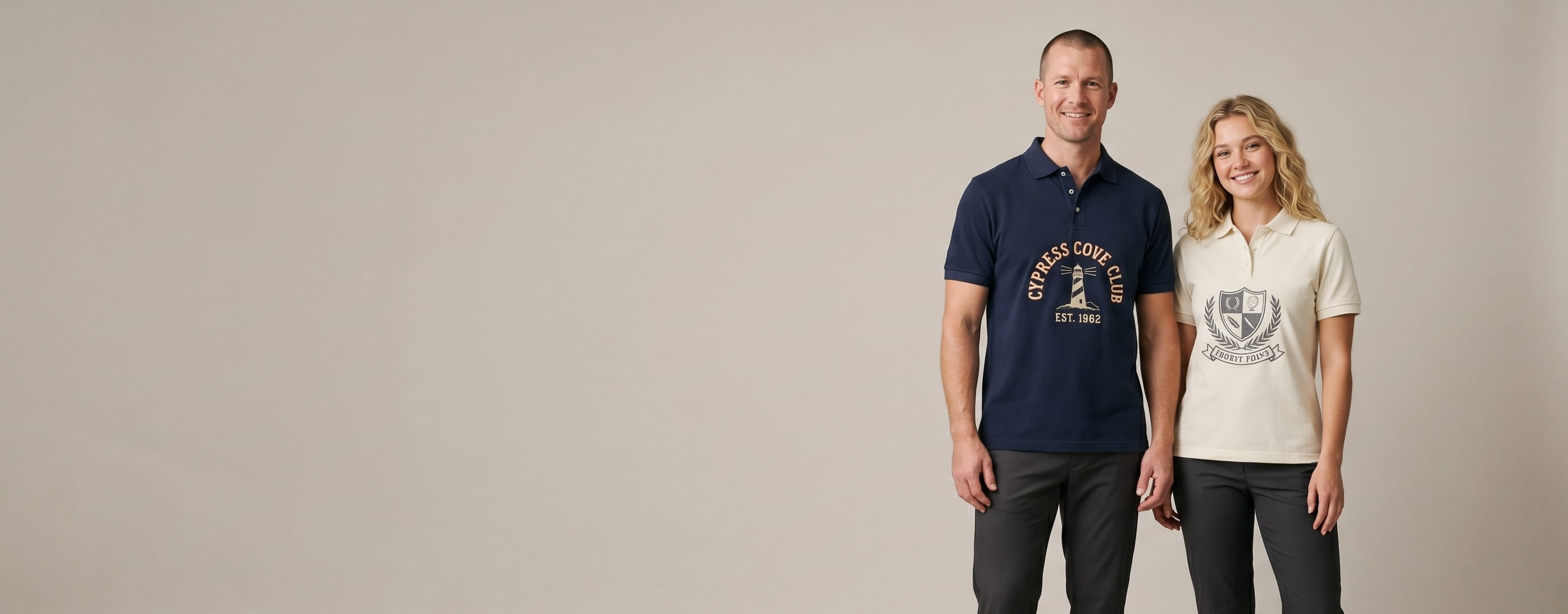 Two lifestyle models in custom embroidered polos — one in a heritage navy cotton-pique short-sleeve polo with a front-chest heritage circle-stamp "CYPRESS COVE CLUB / EST. 1962" flat-embroidered lighthouse emblem, one in a heritage cream cotton-pique short-sleeve polo with a front-chest tonal flat-embroidered country-club shield + chain-stitched "PEBBLE POINT" ribbon banner