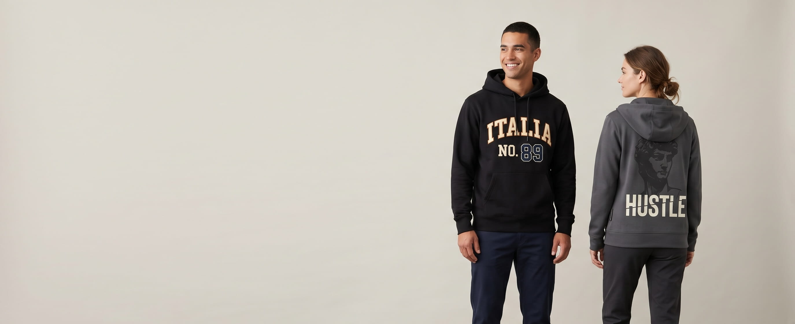 Two lifestyle models in custom Nike hoodies — one in a heritage black Club Fleece pullover with a flat-embroidered "ITALIA / NO. 89" heritage college-varsity arched country wordmark on the chest, one in a dark-smoke-grey Therma-FIT full-zip with a classical-statue + sliced "HUSTLE" typography screen print on the back panel