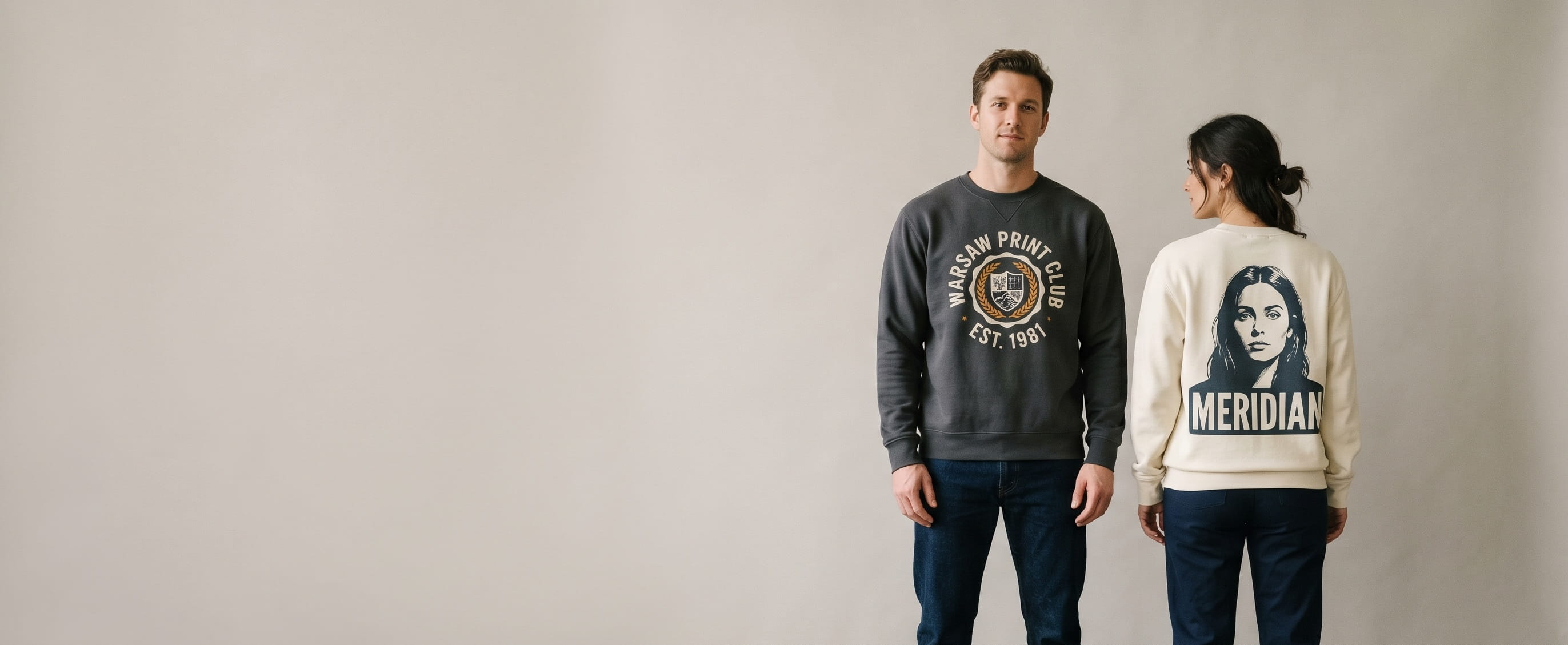 Two lifestyle models in custom printed sweatshirts — one in a heritage charcoal heavyweight ringspun cotton fleece crewneck sweatshirt with a front-chest heritage circle-stamp "WARSAW PRINT CLUB" water-based screen print, one in a heritage cream garment-dyed cotton fleece crewneck sweatshirt with a full-back photo-portrait + bold "MERIDIAN" typography DTG print