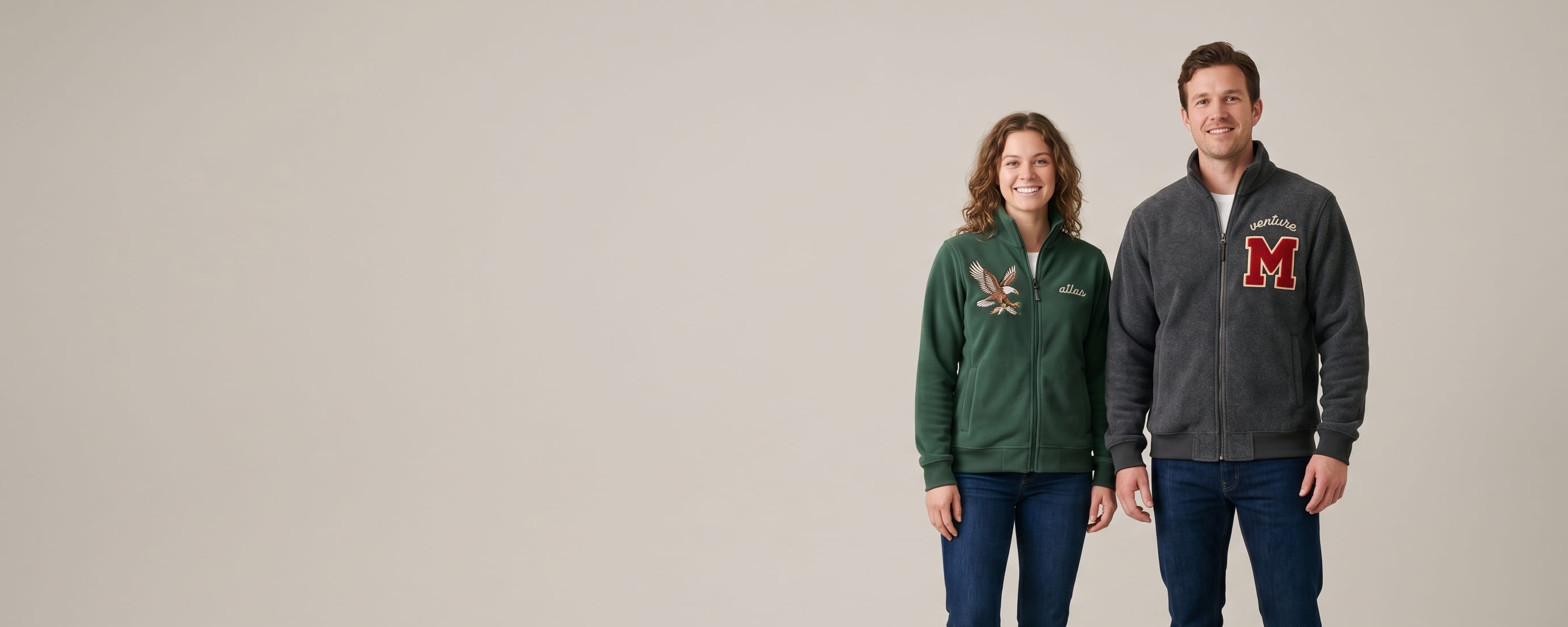 Two lifestyle models in decorated custom fleece jackets — model 1 in charcoal heavyweight fleece jacket with chenille letter patch + chain-stitch embroidery + model 2 in forest-green performance microfleece jacket with heritage flat-embroidered wildlife emblem + tonal embroidery