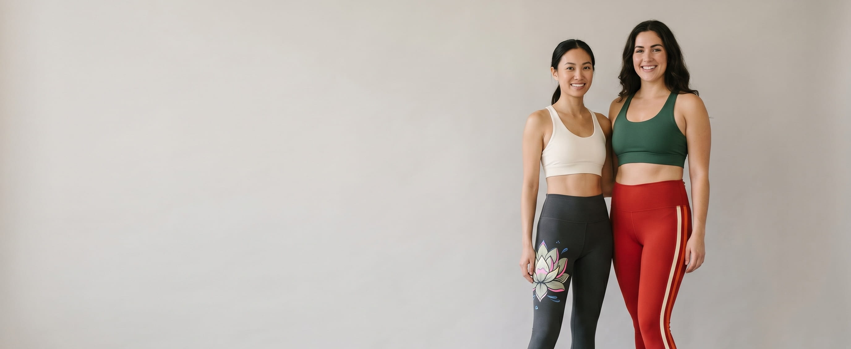 Two women lifestyle models in decorated custom women's leggings — one in anthracite heritage cotton-spandex leggings with a front-thigh full-color DTG composition + one in scarlet polyester performance leggings with a full-leg side-seam tonal-stripe heat-pressed transfer composition