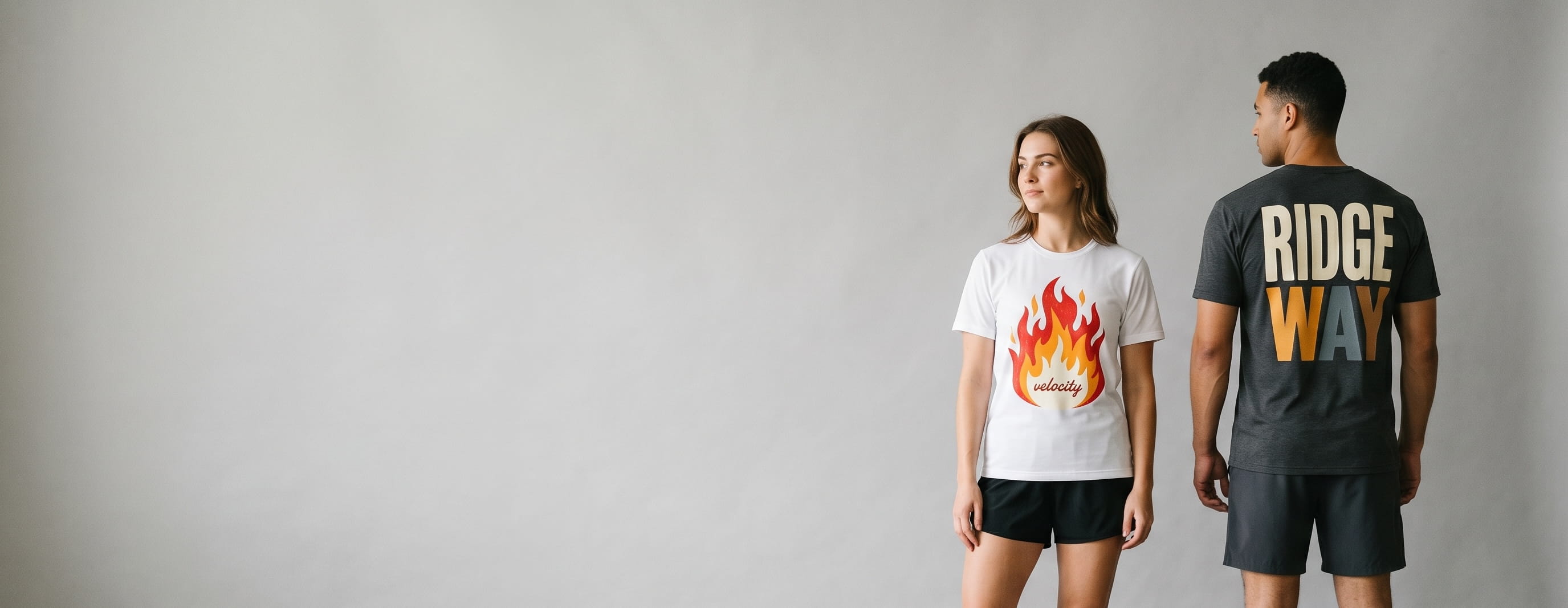 Two lifestyle models in decorated custom performance short-sleeve tees — woman in white performance-jersey tee with bold flame "velocity" front-chest transfer + man in anthracite performance-blend tee with "ridgeway" full-back typography transfer