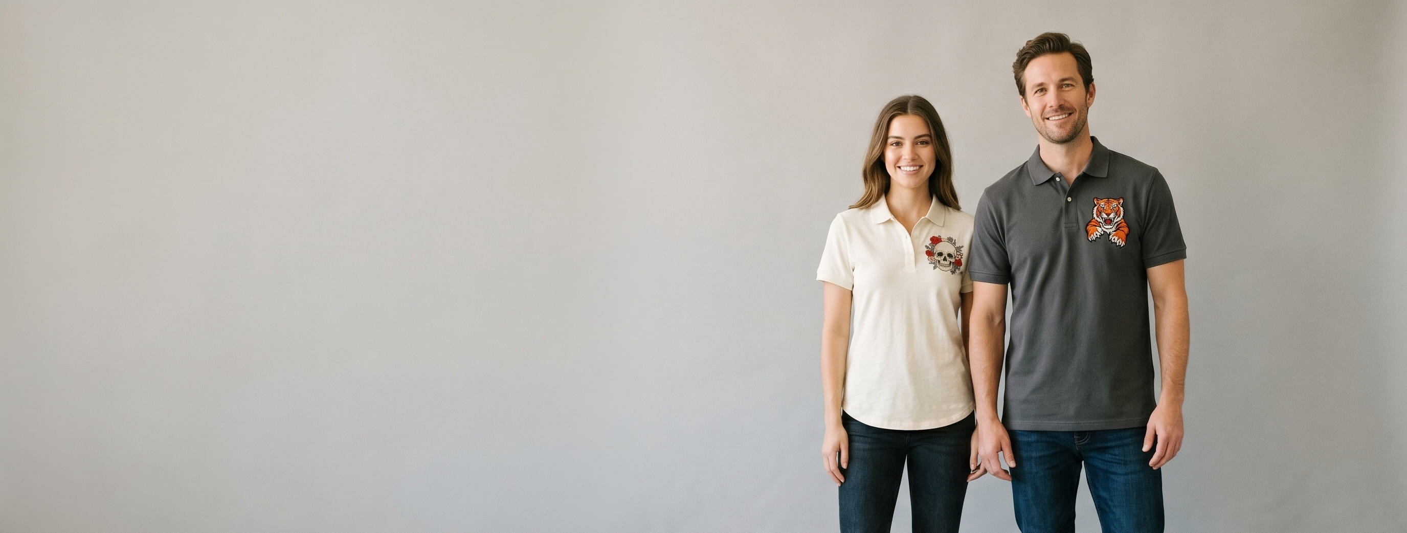 Two lifestyle models in decorated custom polos — one in anthracite pique cotton-blend polo with full-color DTG tiger mascot illustration + one in cream heritage slub-knit polo with heritage flat-embroidered skull + floral bouquet emblem