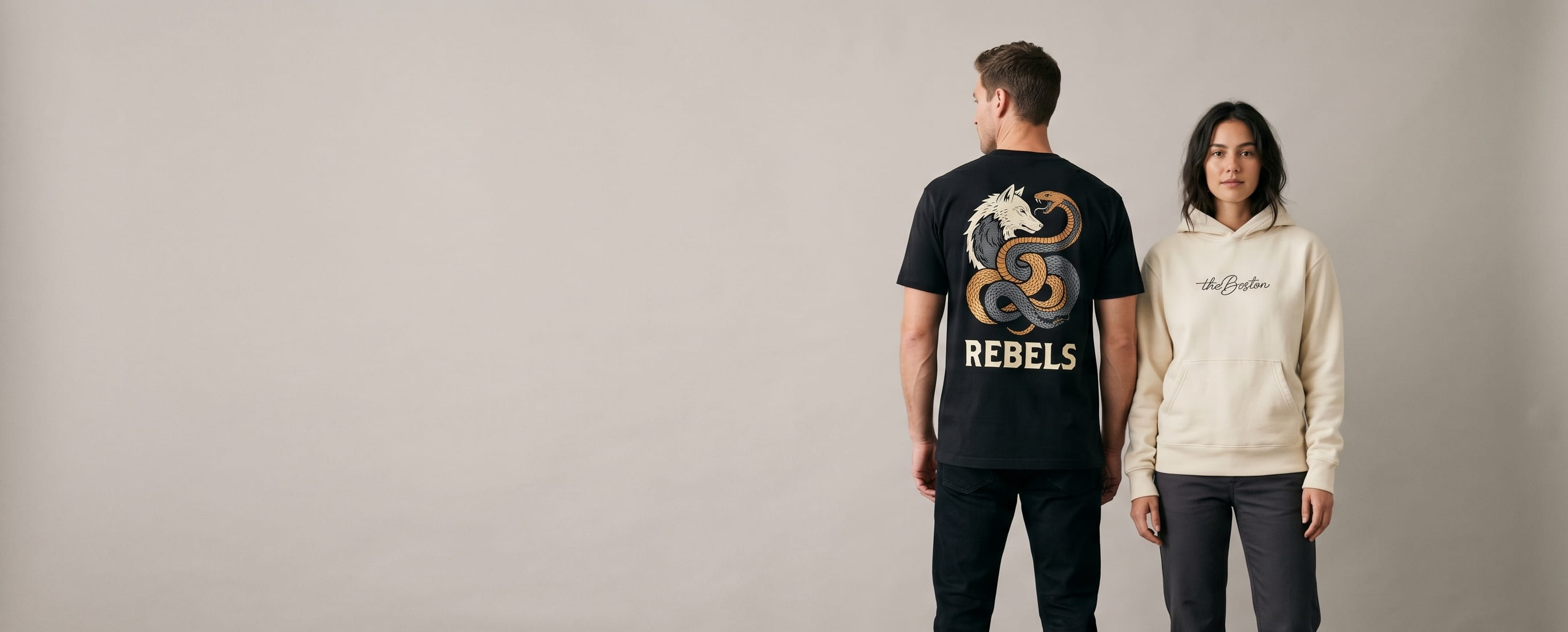 Two lifestyle models in Sales & Deals apparel — one in a heavyweight black cotton tee with a full-chest mythological dual-creature DTG print, one in a heritage cream cotton hoodie with a small tonal flat-embroidered script-signature monogram at the chest