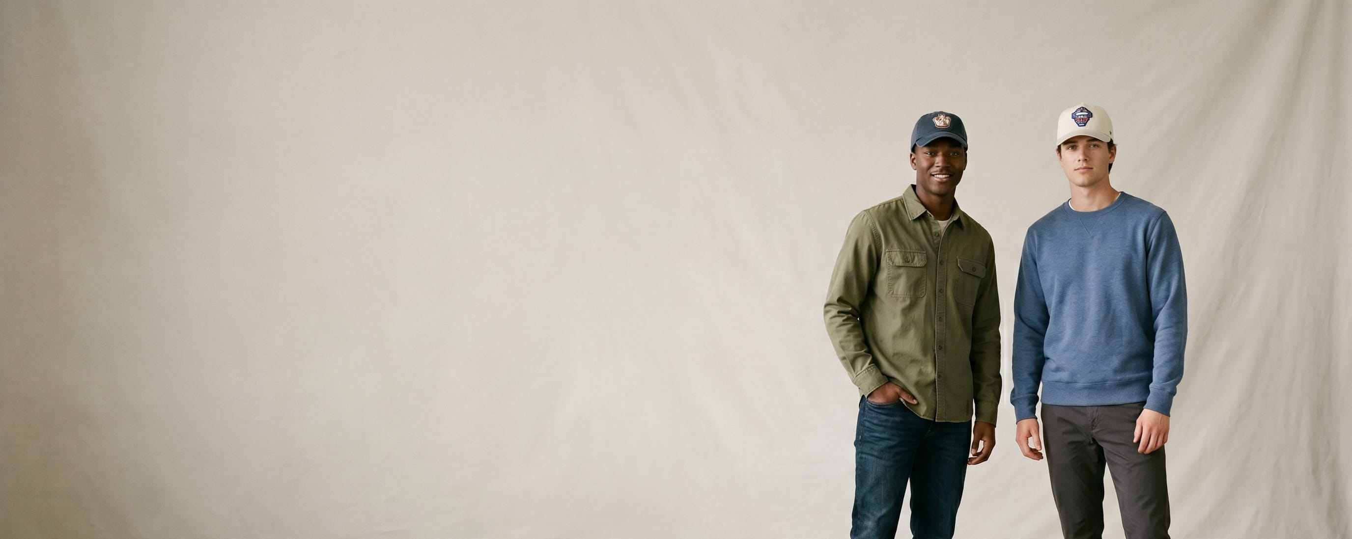 Two sports-lifestyle models wearing decorated 47 Brand caps — a front-crown vintage baseball-glove embroidery on the first man's navy Clean Up dad hat and a front-crown catcher's-mask 3D puff on the second man's cream MVP structured cap