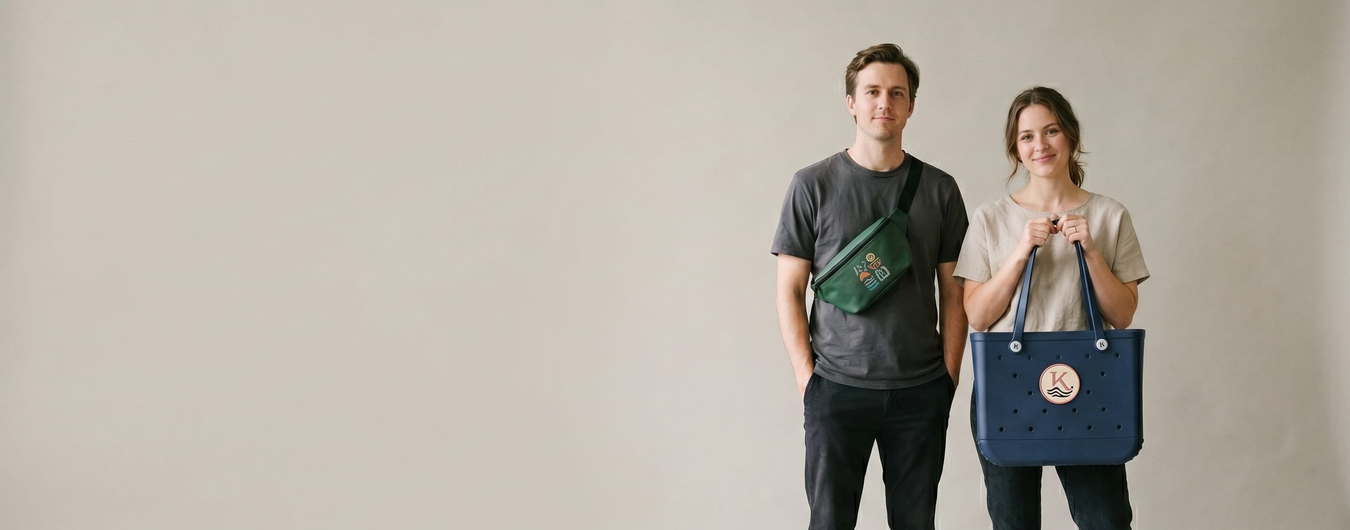 Two lifestyle models carrying personalized Bogg bags — a woven-patch monogram crest on the woman's navy Original tote and a heat-pressed transfer roundel on the man's forest-green Belt Bag
