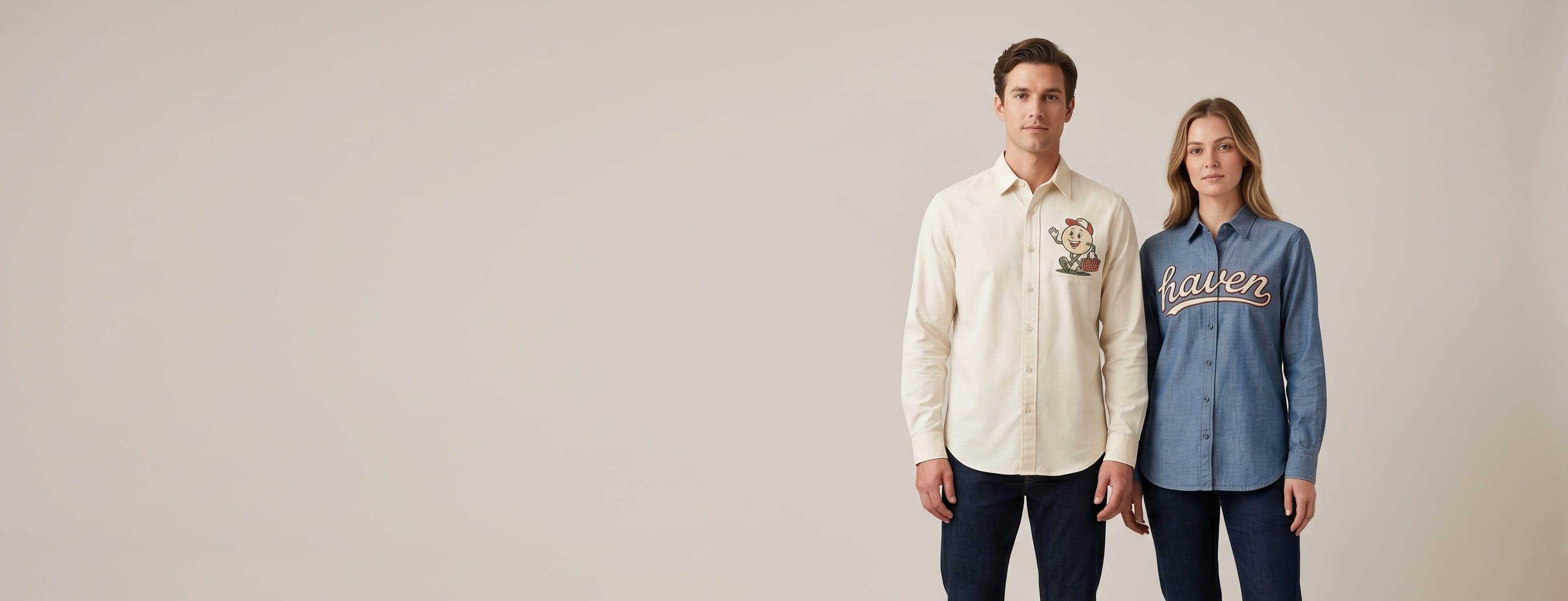 Two lifestyle models in decorated custom button-up shirts — one in cream premium cotton-stretch twill button-up with heritage flat-embroidered vintage cartoon mascot emblem + one in indigo heritage chambray button-up with heritage chain-stitch embroidery wordmark