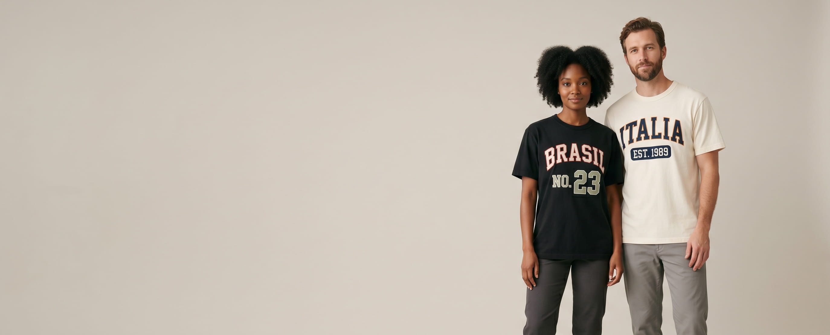 Two lifestyle models in custom embroidered tees — one in a heavyweight cream ringspun cotton tee with a high-density flat-embroidered "ITALIA / EST. 1989" heritage athletic stacked country wordmark, one in a heavyweight black garment-dyed cotton tee with a flat-embroidered "BRASIL / NO. 23" varsity country and jersey-number composition