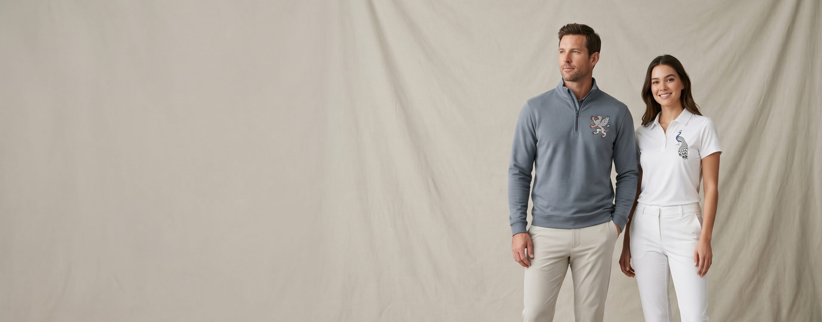 Two premium golf-lifestyle models wearing decorated G Fore — a heraldic-griffin left-chest embroidery on the man's slate-grey brushed-back tech terry quarter-zip and a peacock left-chest heat-press transfer on the woman's snow-white silky tech nylon polo