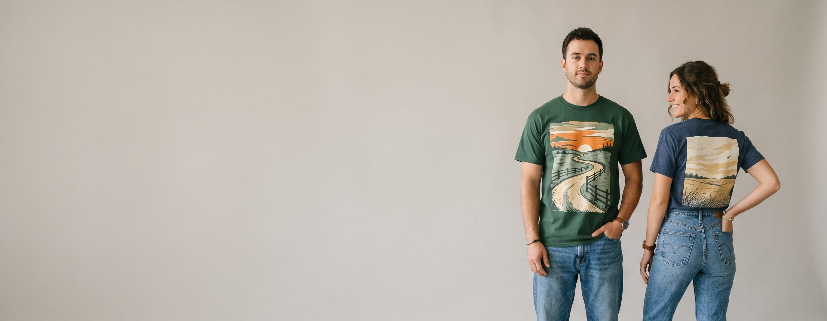 Two everyday-lifestyle models wearing decorated Gildan tees — a large full-front country-road sunset scenic screen print on the man's forest-green Heavy Cotton tee, with the woman turned to show a large full-back prairie golden-hour scenic heat-press transfer on her heather-navy Softstyle tee