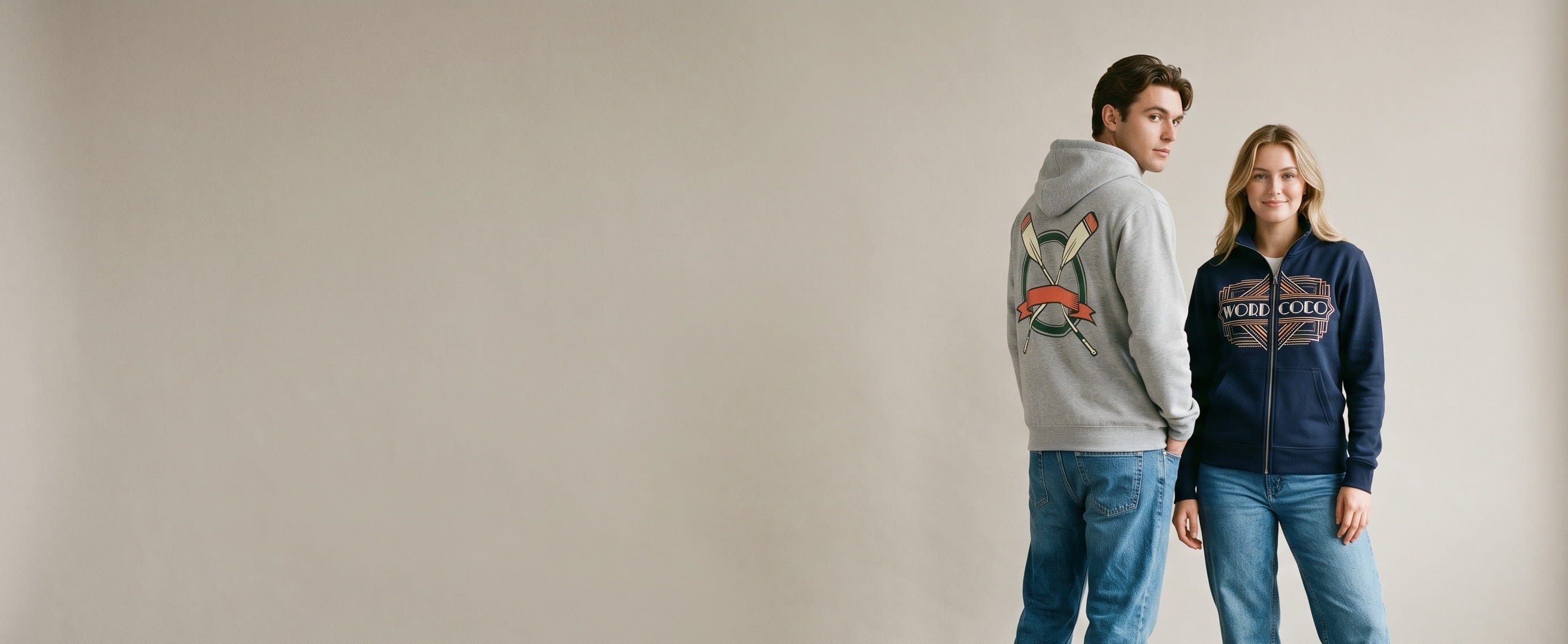 Two campus lifestyle models wearing decorated Just Hoods by AWDis — full-back crossed rowing-oars plastisol screen print on the man's heather-grey midweight college pullover hoodie and an art-deco wordmark full-color DTG on the woman's french-navy college full-zip hoodie