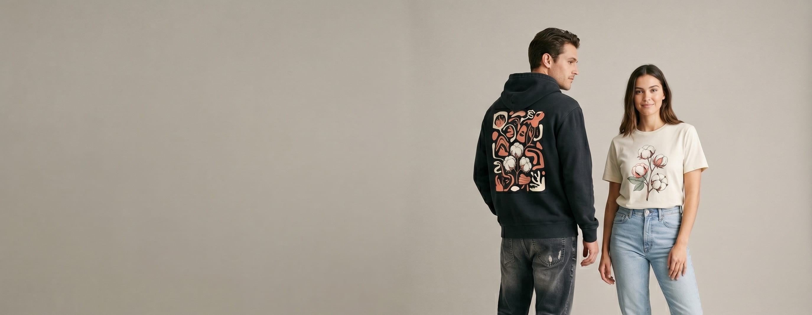 Two premium-basics lifestyle models wearing decorated Original Favorites — a full-back condensed-serif headline-wordmark screen print on the man's washed-black organic-cotton hoodie and a cotton-boll full-color DTG on the woman's natural-ecru Supima cotton crew tee