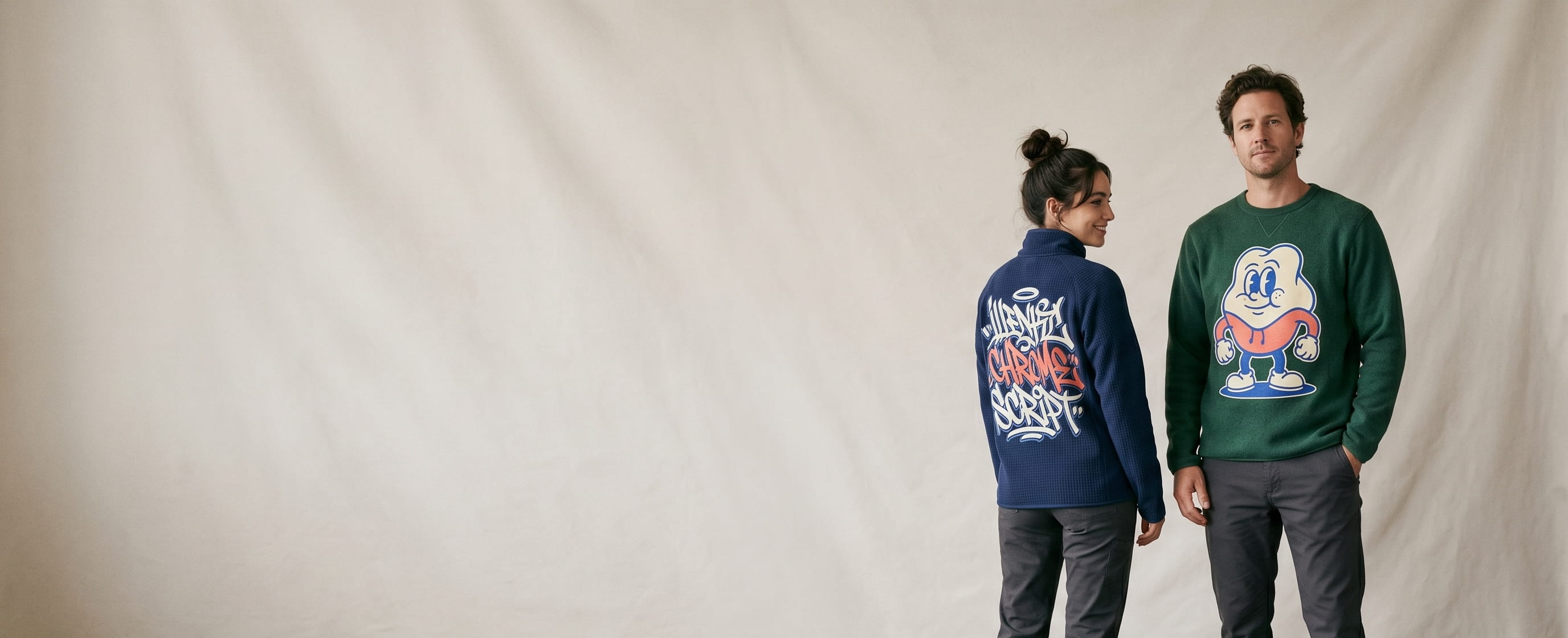 Two outdoor-lifestyle models wearing decorated Patagonia outerwear — a large full-front cartoon-mascot plastisol screen print on the man's forest-green recycled fleece pullover, with the woman turned to show a large full-back graffiti chrome wordmark heat-pressed transfer on her deep-navy fleece quarter-zip