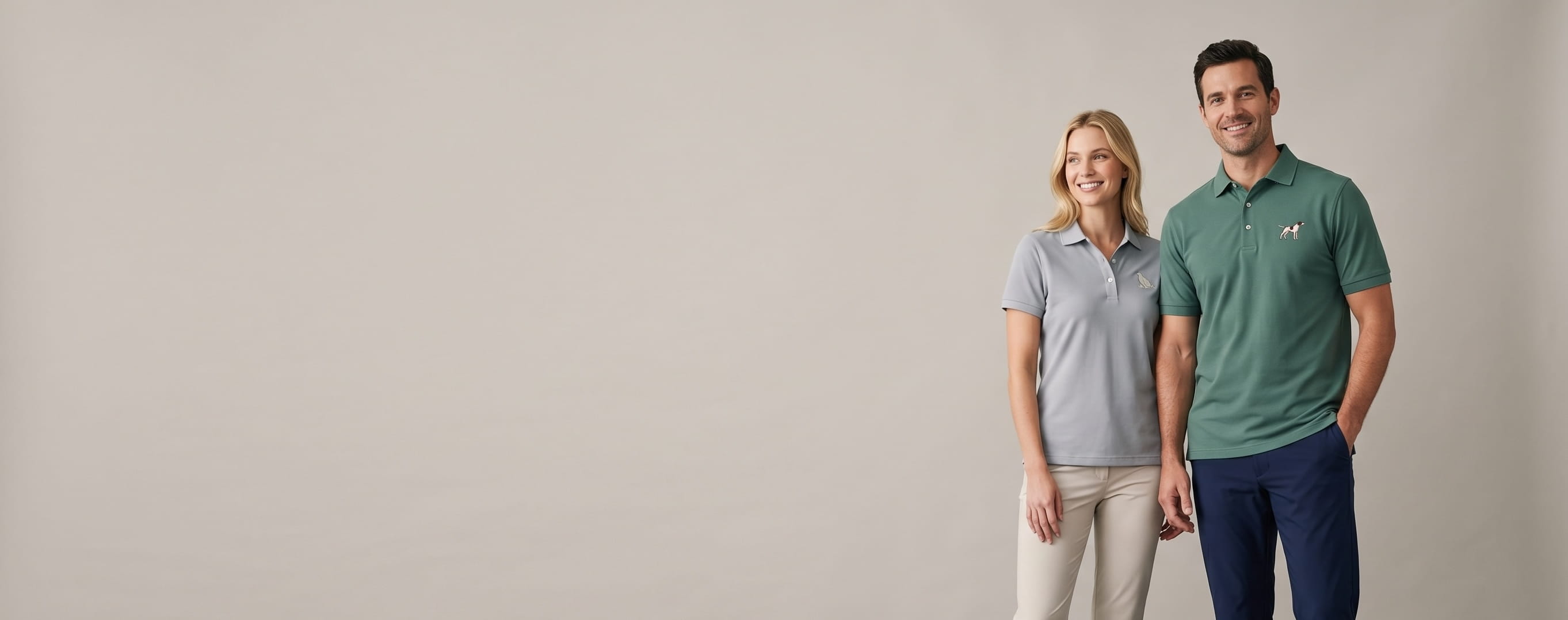 Two golf-lifestyle models wearing decorated Peter Millar apparel — a refined left-chest pointer gun-dog embroidery on the man's juniper-green performance pique polo, with the woman in a gale-grey polo showing a left-chest bobwhite-quail tonal embroidery