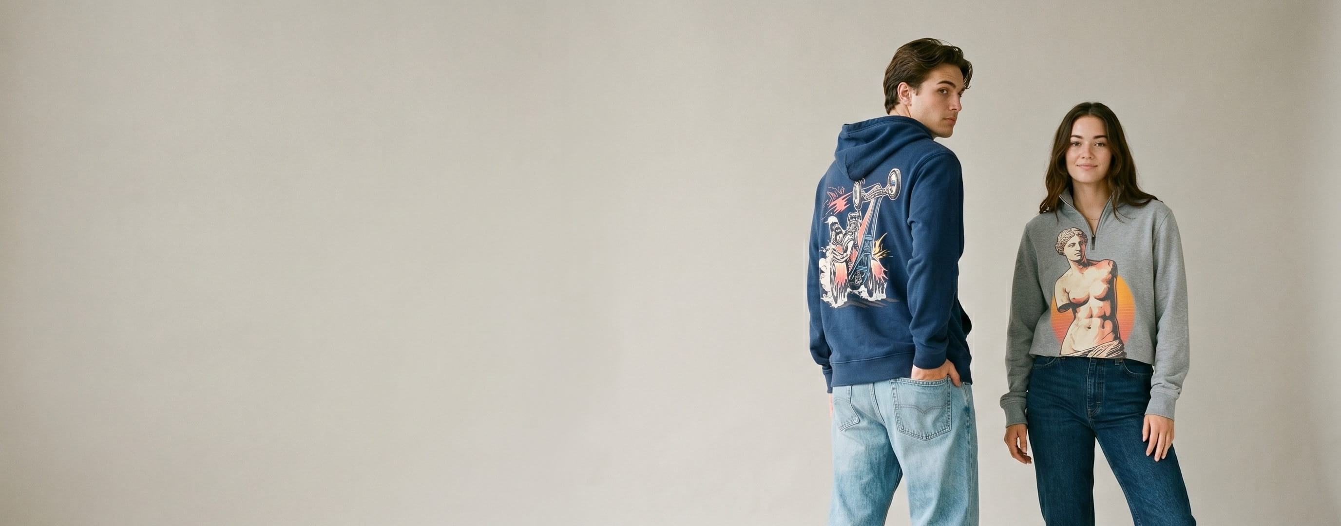 Two lifestyle models wearing decorated Vineyard Vines — a full-back dragster plastisol screen print on the man's vineyard-navy Vineyard Terry hoodie and a venus-de-milo statue full-color DTG on the woman's crew-grey Dreamcloth shep quarter-zip