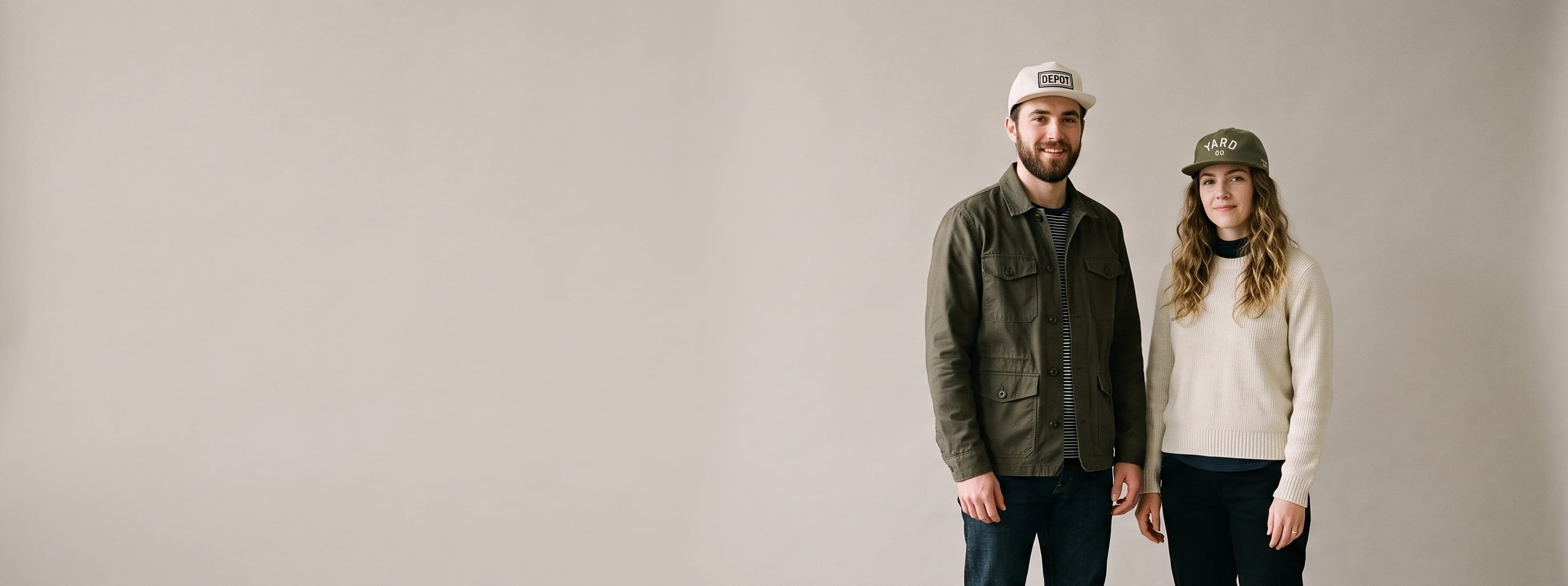Two lifestyle models in decorated custom five-panel camp caps — man in a natural cotton-twill 5-panel with a centered woven label patch + woman in a nylon camp cap with a flat-embroidered emblem on the seamless front panel
