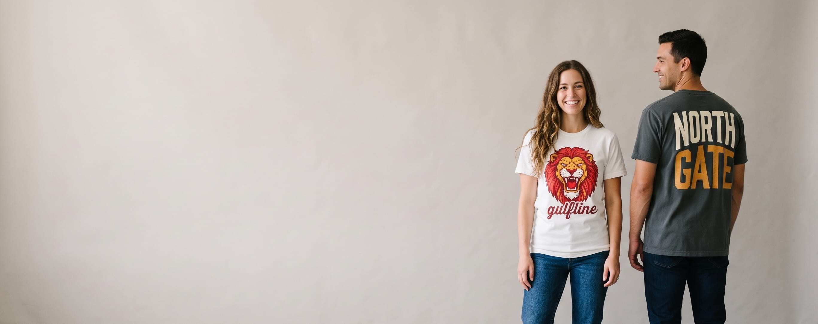 Two lifestyle models in decorated custom short-sleeve cotton tees — woman in a white ringspun-cotton tee with a full-chest screen print + man in an anthracite heavyweight garment-dyed tee with a full-back screen print