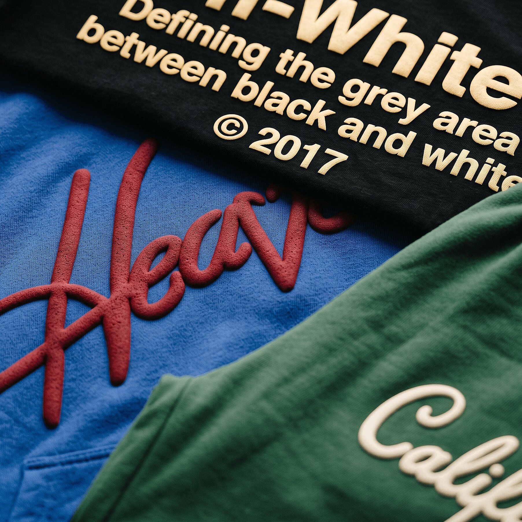 Flat-lay of bold raised 3D puff-printed tees, hoodies, and sweatpants